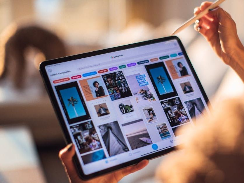 Hands holding a tablet showing a photo gallery, with a stylus hovering over the screen.