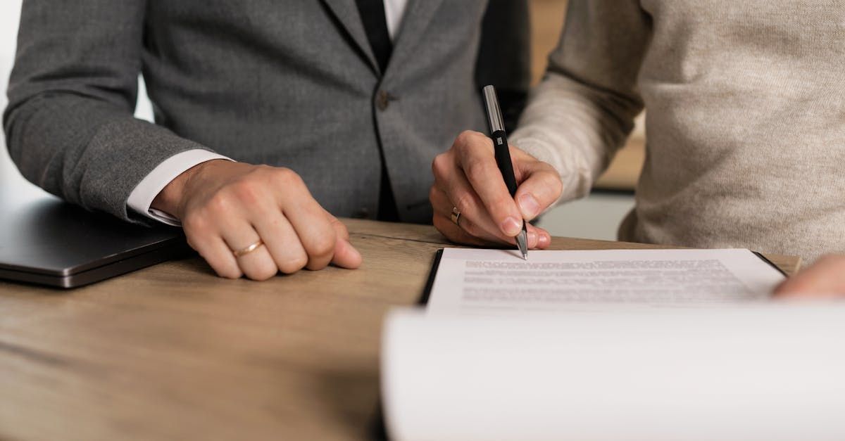 Two people in business attire signing a document at a desk