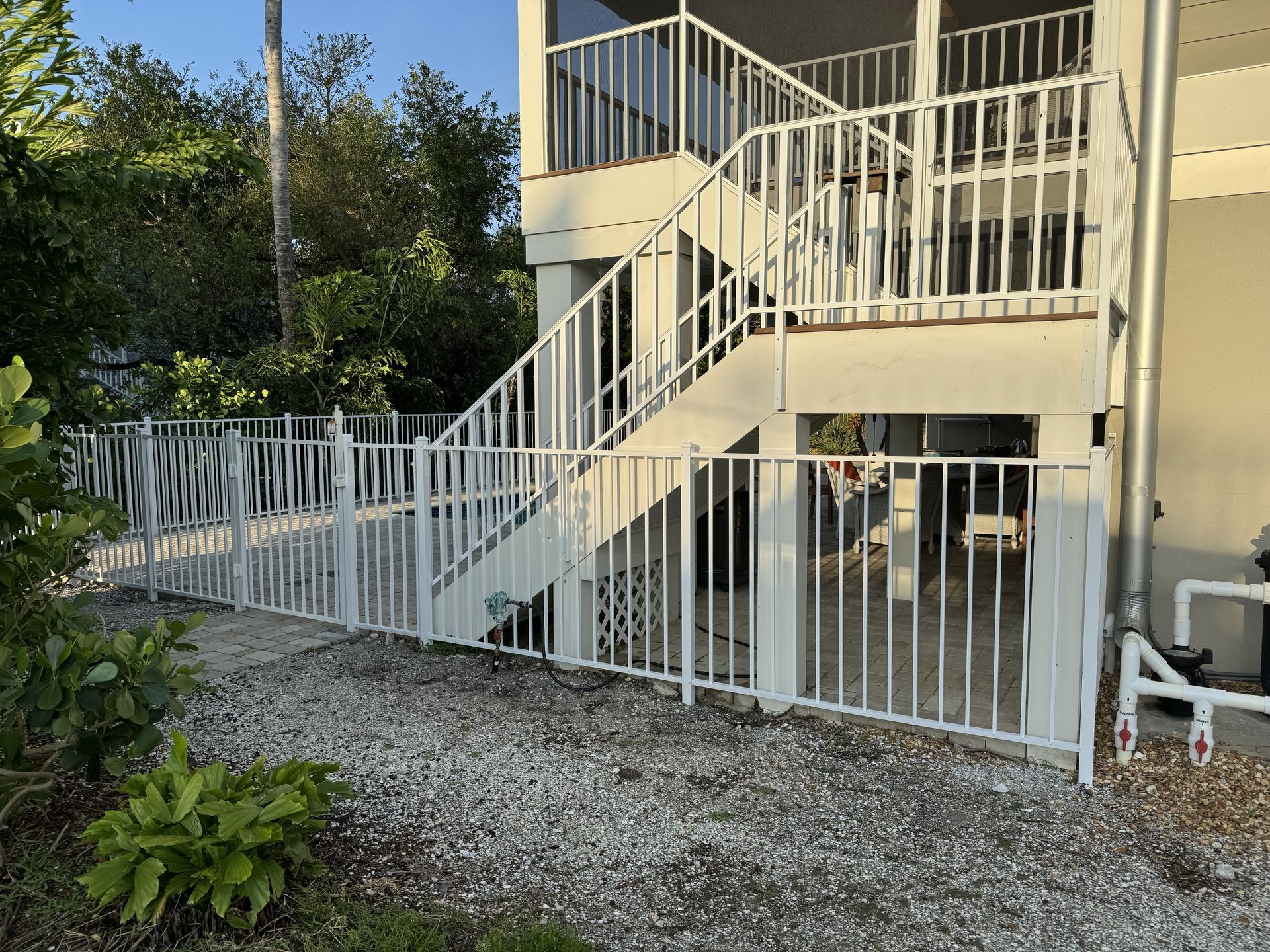 A white fence surrounds a house with stairs leading up to it.