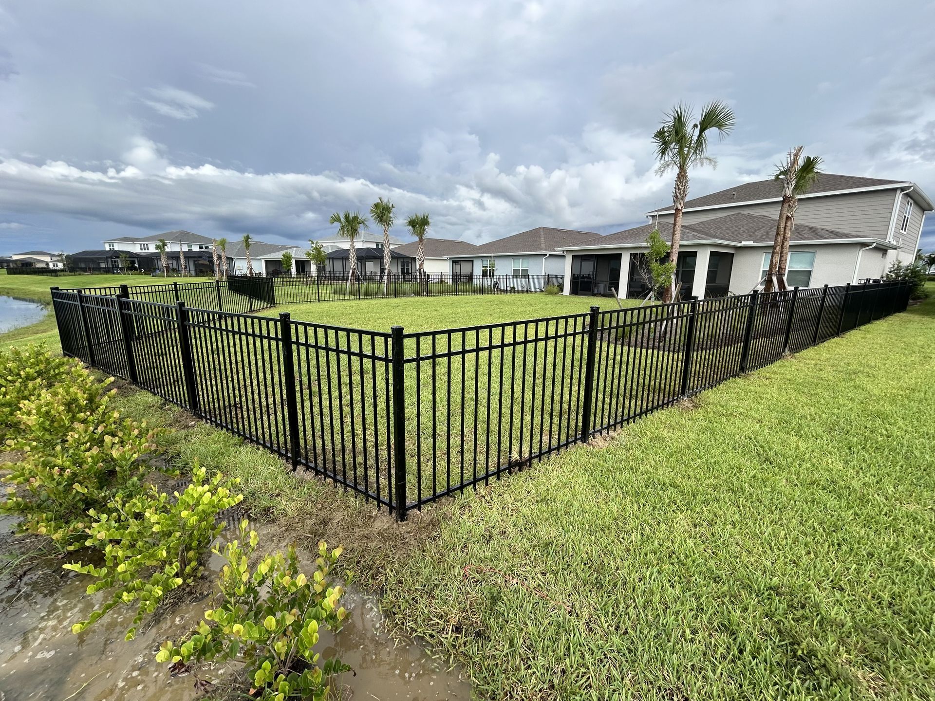 A black fence surrounds a lush green field in front of a house.
