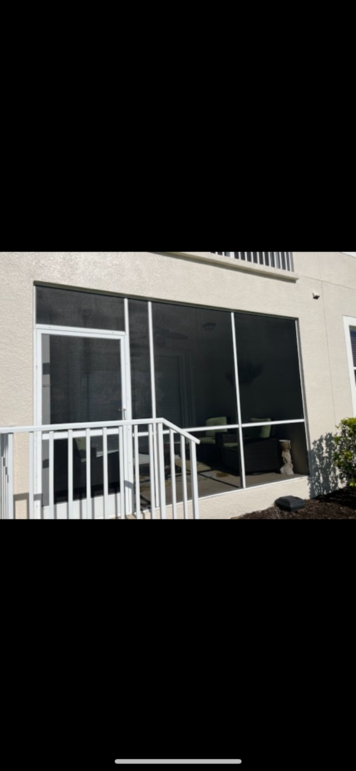 A screened in porch with a white railing and sliding glass doors.