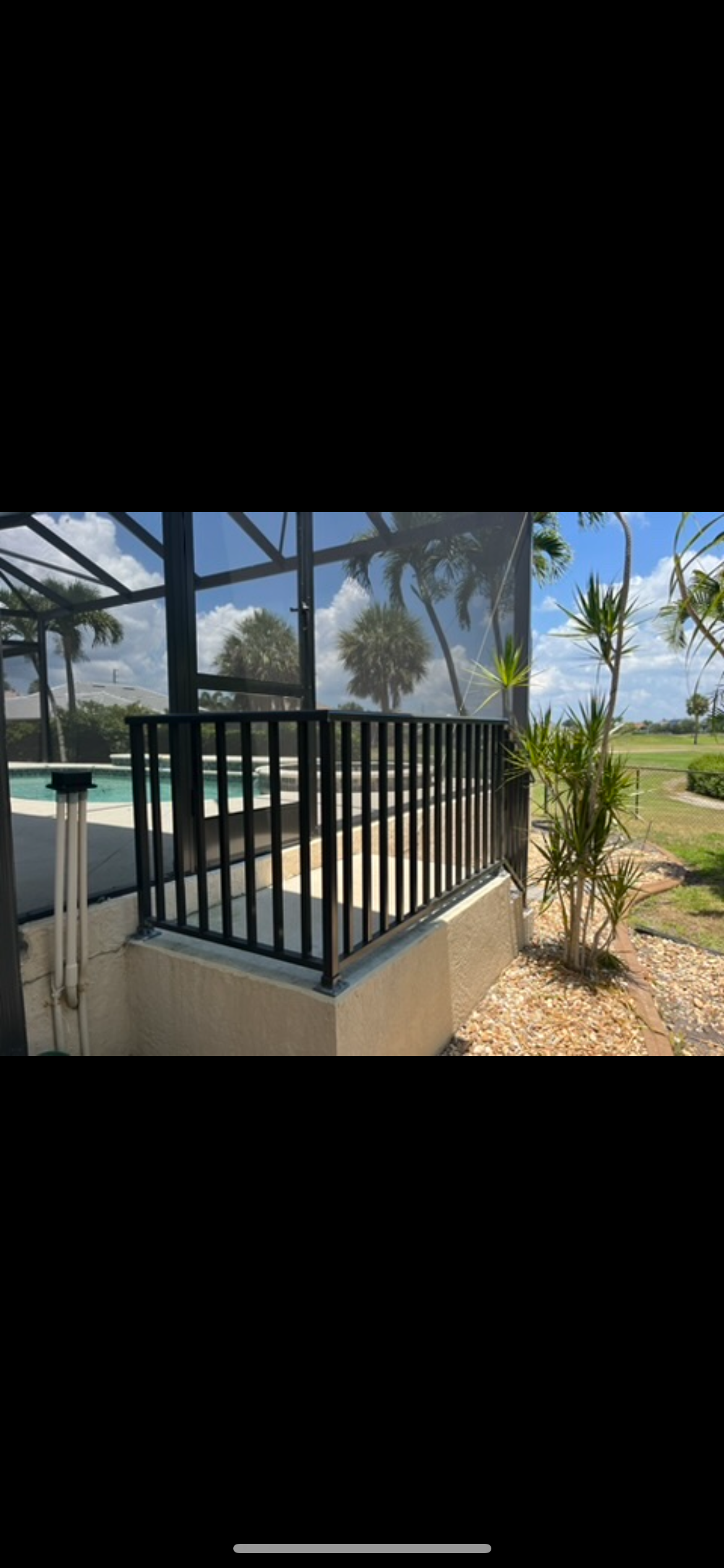 A screened in porch with a railing and a view of a pool.