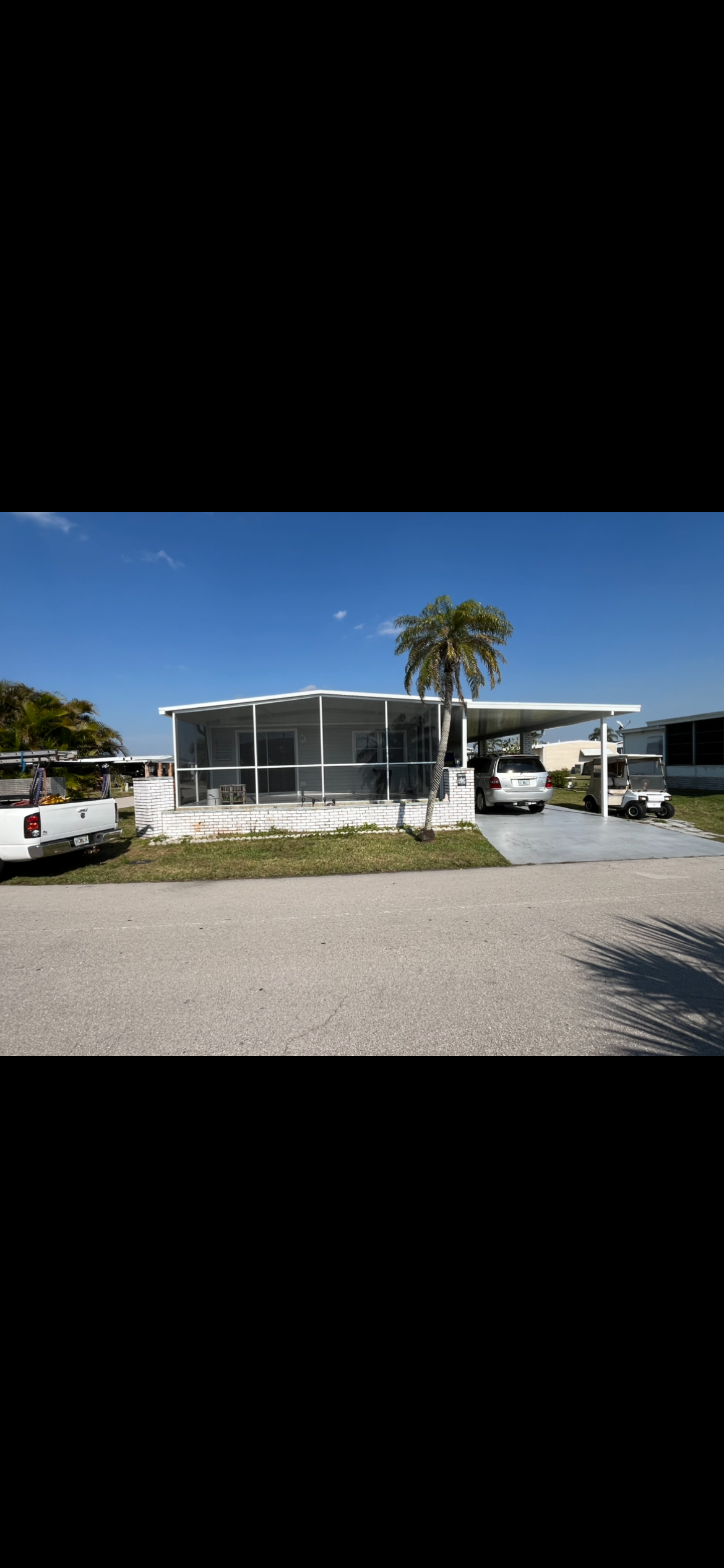 A mobile home with a screened in porch and a palm tree in front of it.