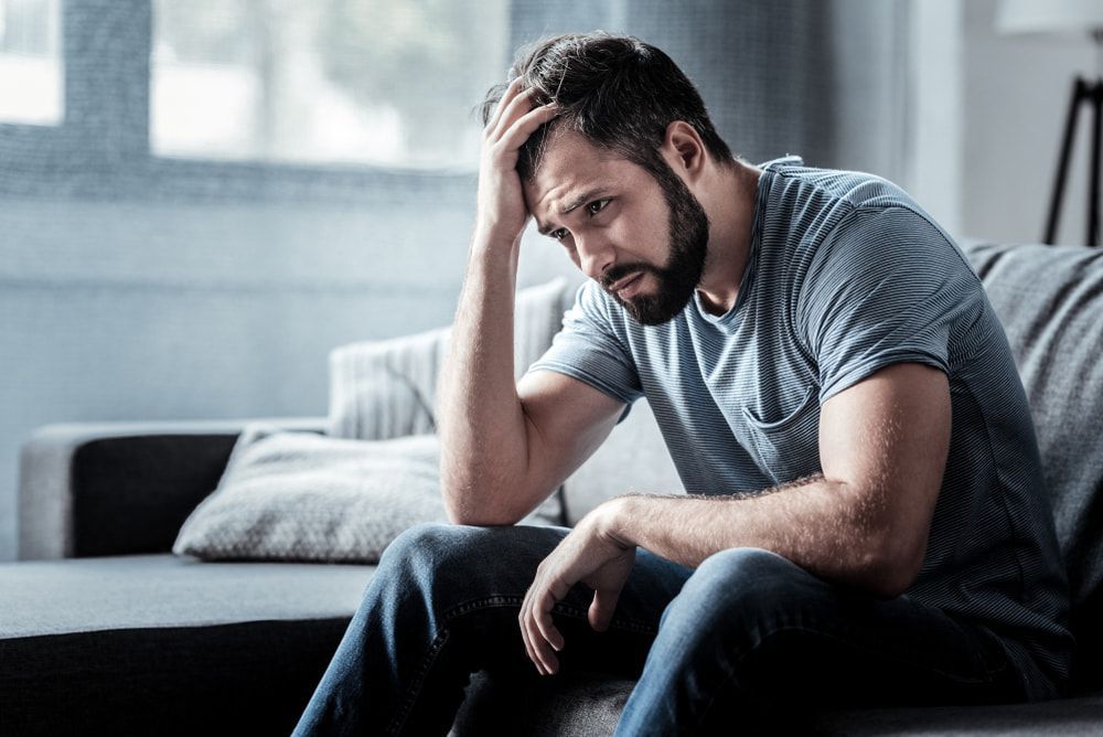 A Sad Man Sitting On A Couch With His Hand On His Head — Naturopath Australia In Mermaid Beach, QLD