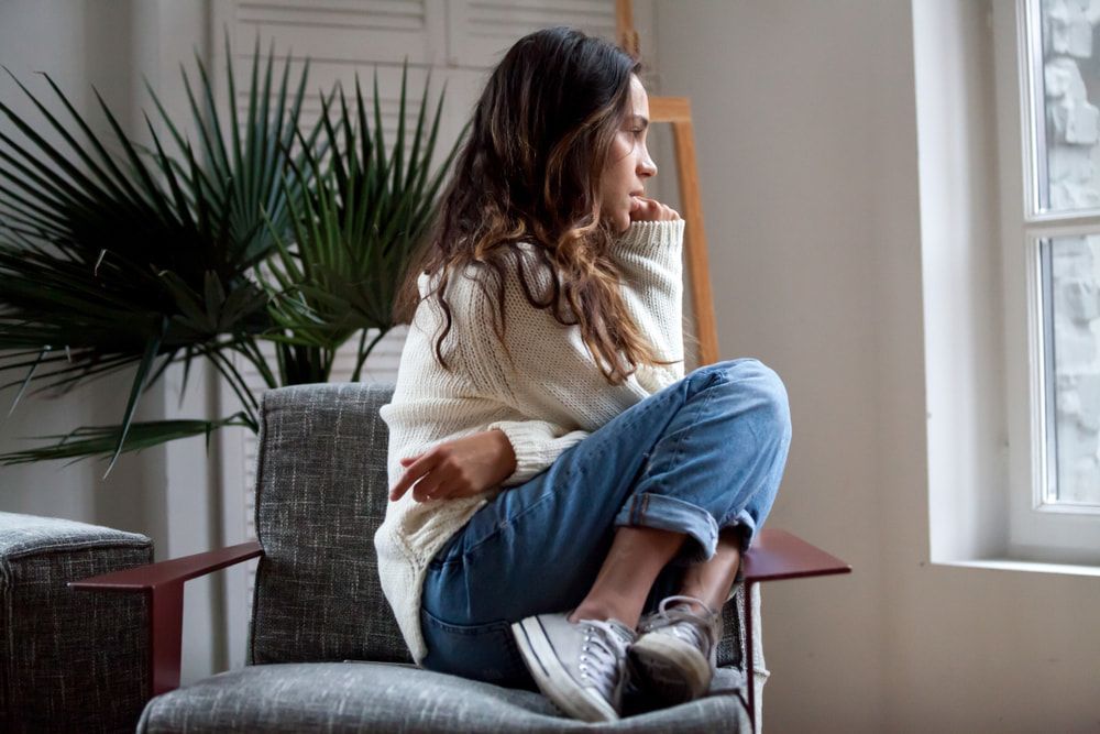 A Woman Is Sitting In A Chair Looking Out A Window — Naturopath Australia In Byron Bay, NSW