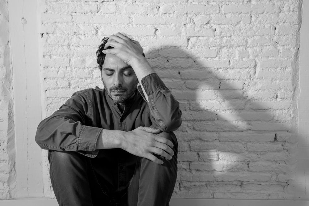 A Man Is Sitting In Front Of A Brick Wall With His Hands On His Head — Naturopath Australia In Mermaid Beach, QLD