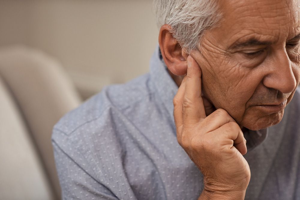 An Older Man Is Sitting On A Couch With His Hand On His Ear — Naturopath Australia In Mermaid Beach, QLD