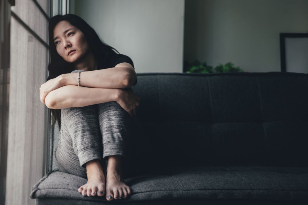 A Sad Woman Sits On A Couch Looking Out A Window — Naturopath Australia In Mermaid Beach, QLD