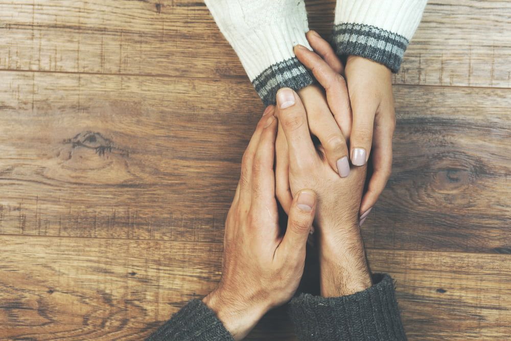A Man And A Woman Are Holding Hands On A Wooden Table — Naturopath Australia In Mermaid Beach, QLD