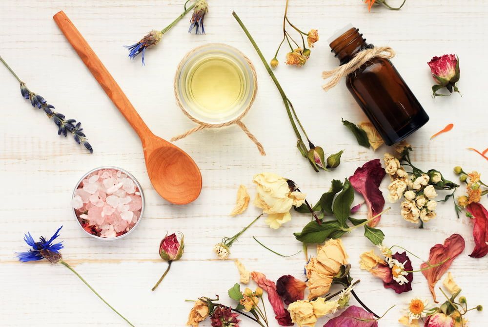 A Bottle Of Essential Oil Surrounded By Dried Flowers And A Wooden Spoon — Naturopath Australia In  Mermaid Beach, QLD
