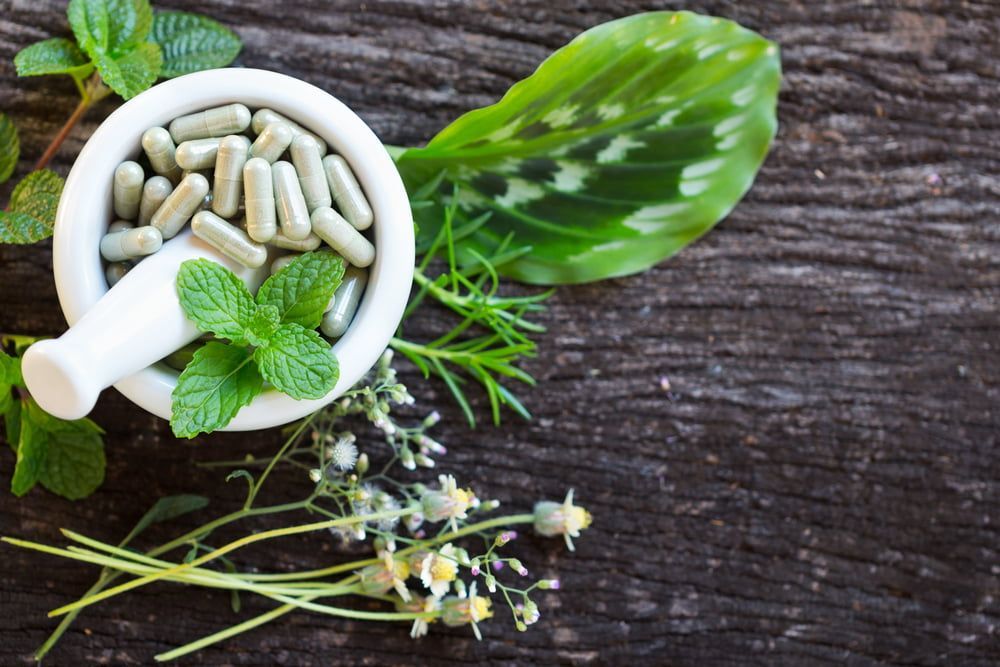 A Mortar And Pestle Filled With Herbs And Capsules — Naturopath Australia In Mermaid Beach, QLD