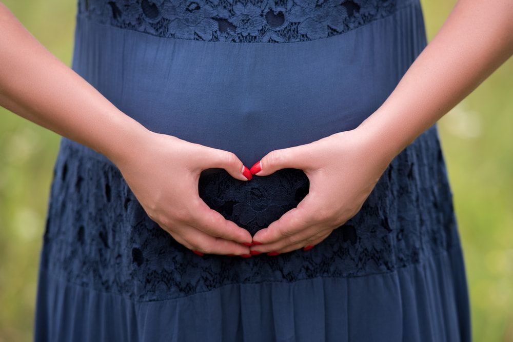 A Woman In A Blue Dress Is Making A Heart Shape With Her Hands Above Her Stomach — Naturopath Australia In Mermaid Beach, QLD