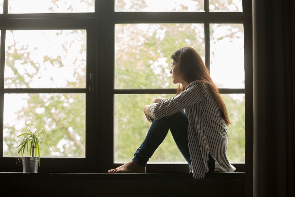 A Woman Is Sitting On A Window Sill Looking Out The Window — Naturopath Australia In Mermaid Beach, QLD