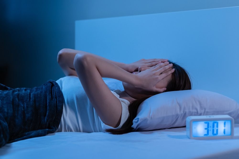 A Woman Laying On A Bed Next To An Alarm Clock — Naturopath Australia In Mermaid Beach, QLD
