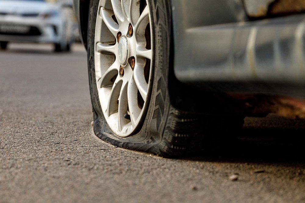 Car tire with a flat, deflated sidewall on a car parked on the road.