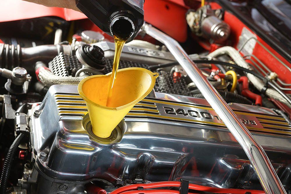 Oil being poured into a car engine through a yellow funnel in a red engine bay