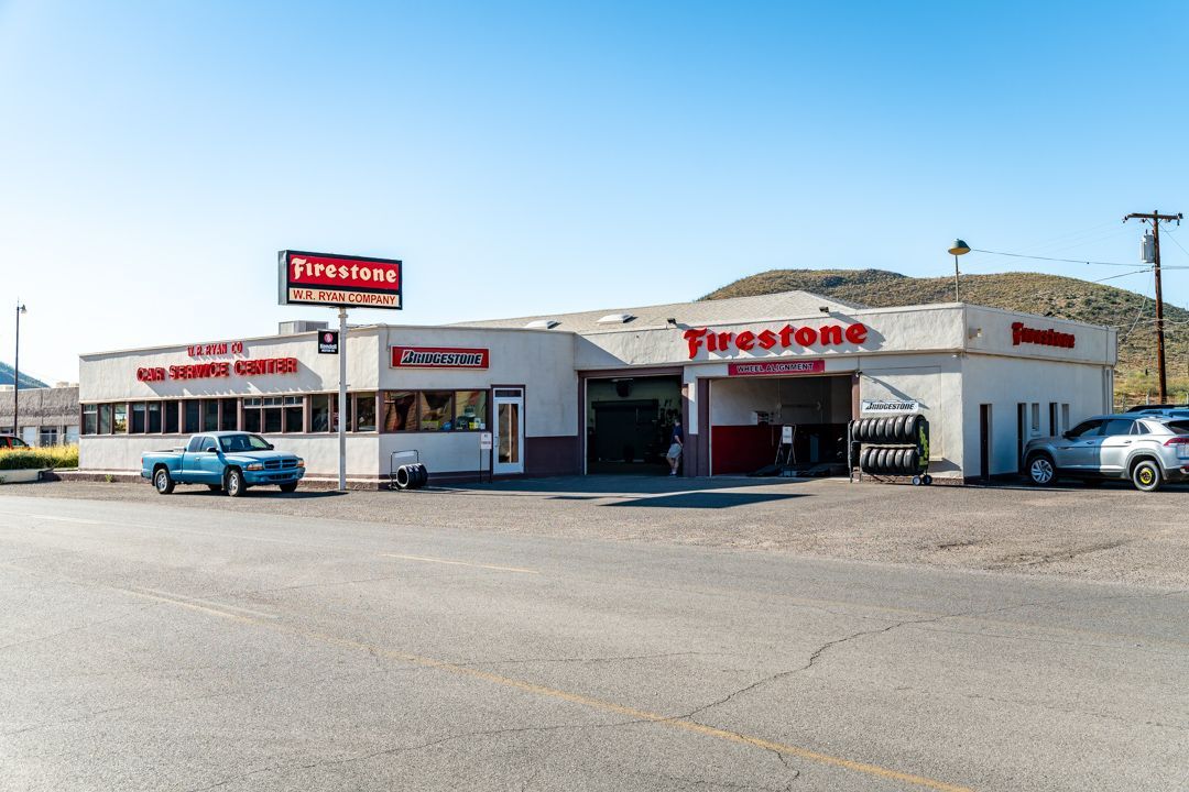 Firestone auto service shop on a sunny street, with parked cars and a large red Firestone sign