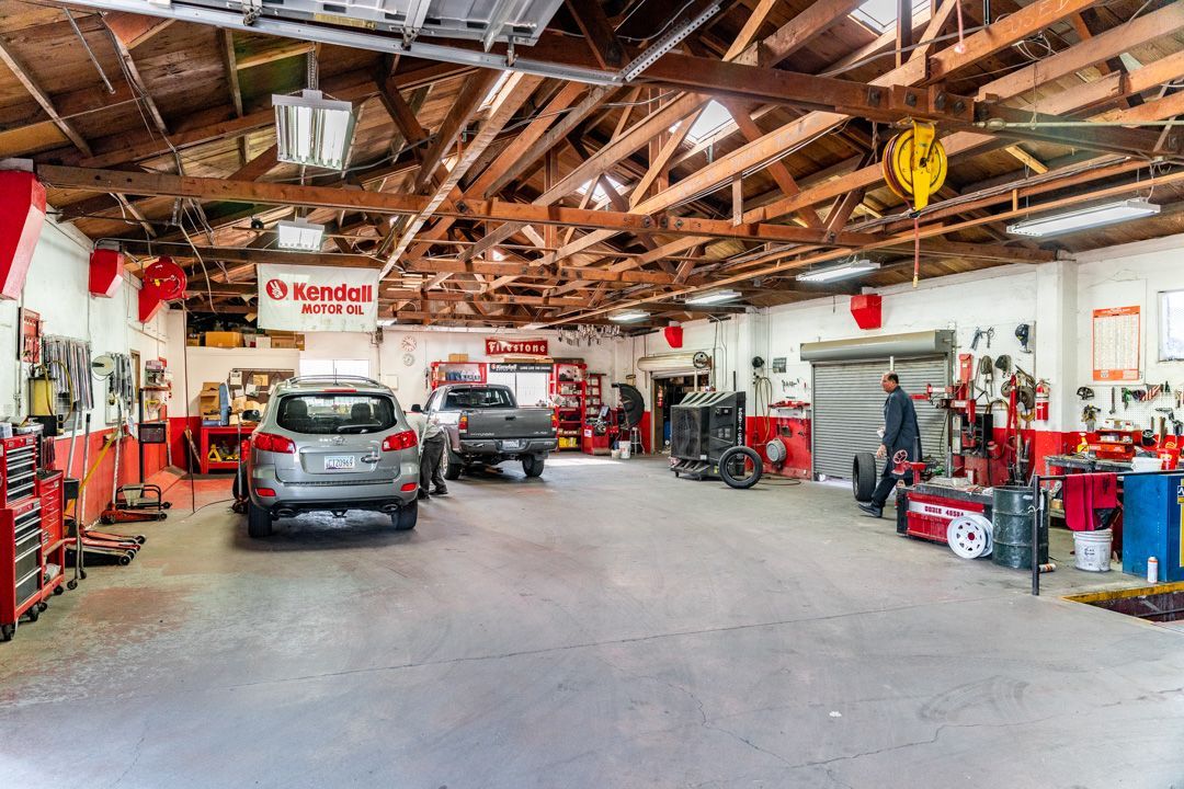 Auto repair shop interior with two cars, tools, and equipment under exposed wooden rafters