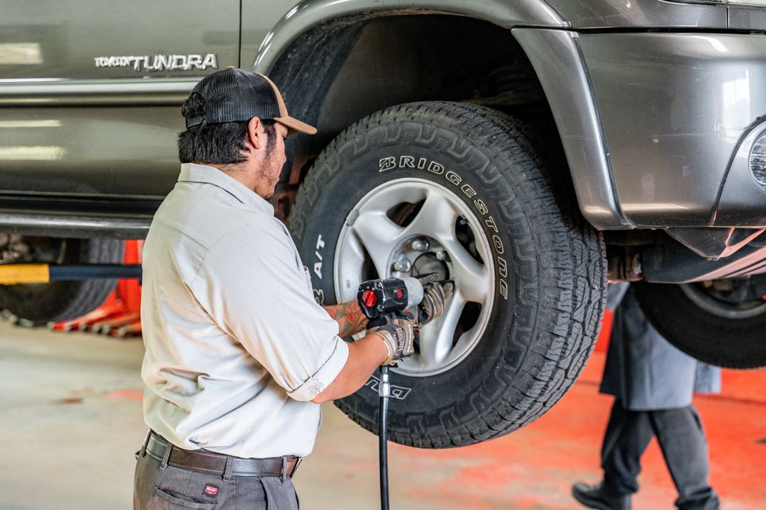 Mechanic using an impact wrench to remove a tire from a gray SUV in a garage.