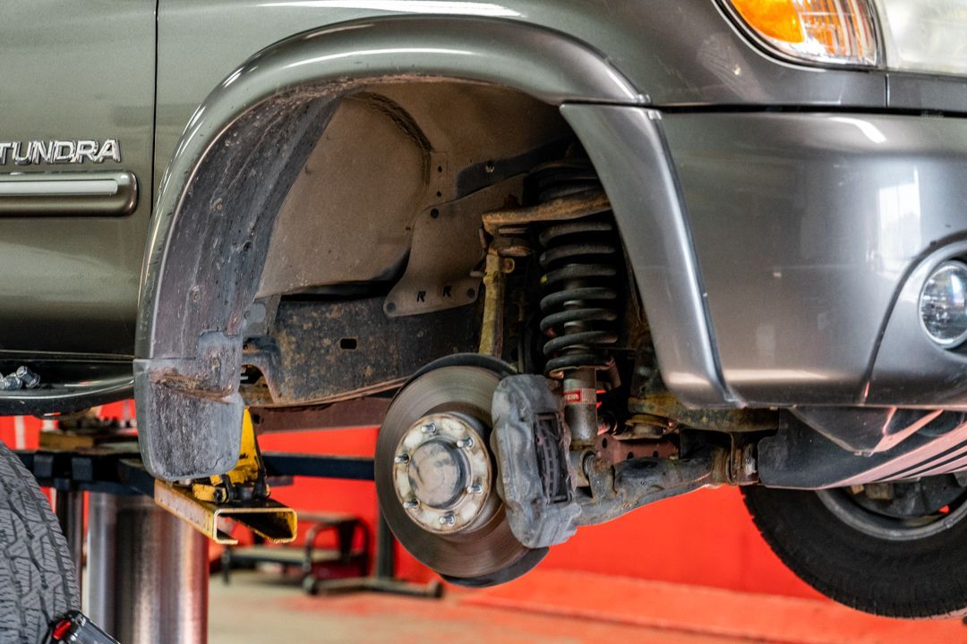 Car’s front wheel and suspension exposed on a lift in an auto repair shop