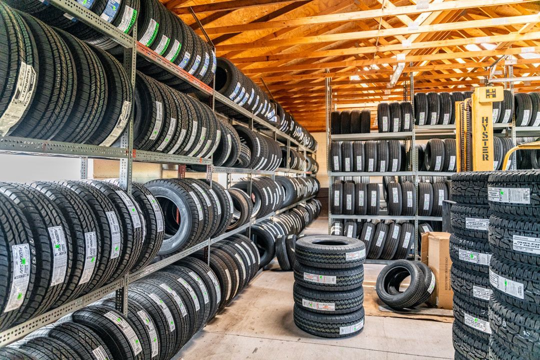 Stacked tires in a warehouse workshop with rows of shelves and a wooden roof.