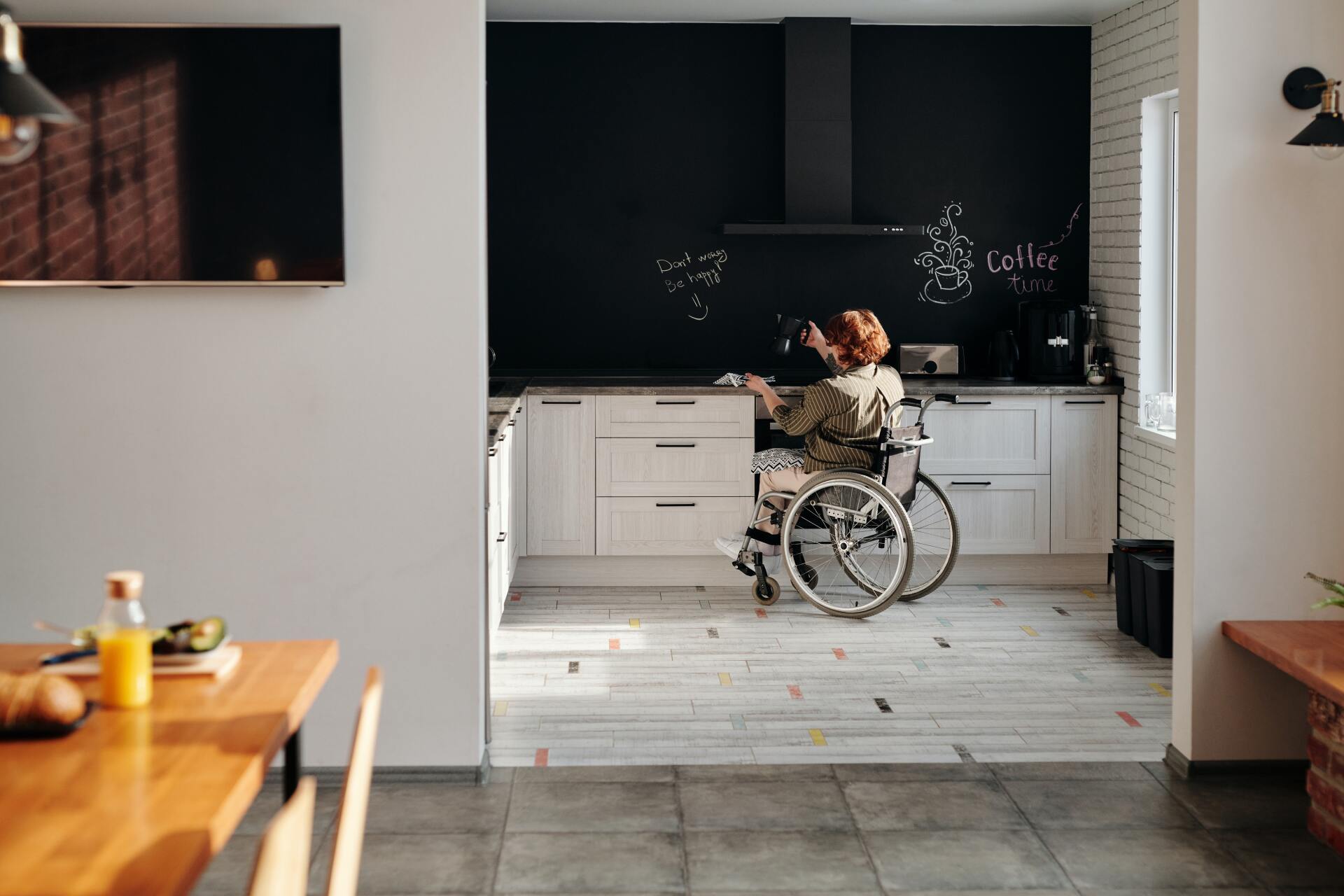 why you should invest in NDIS housing A woman in a wheelchair is sitting in a kitchen.