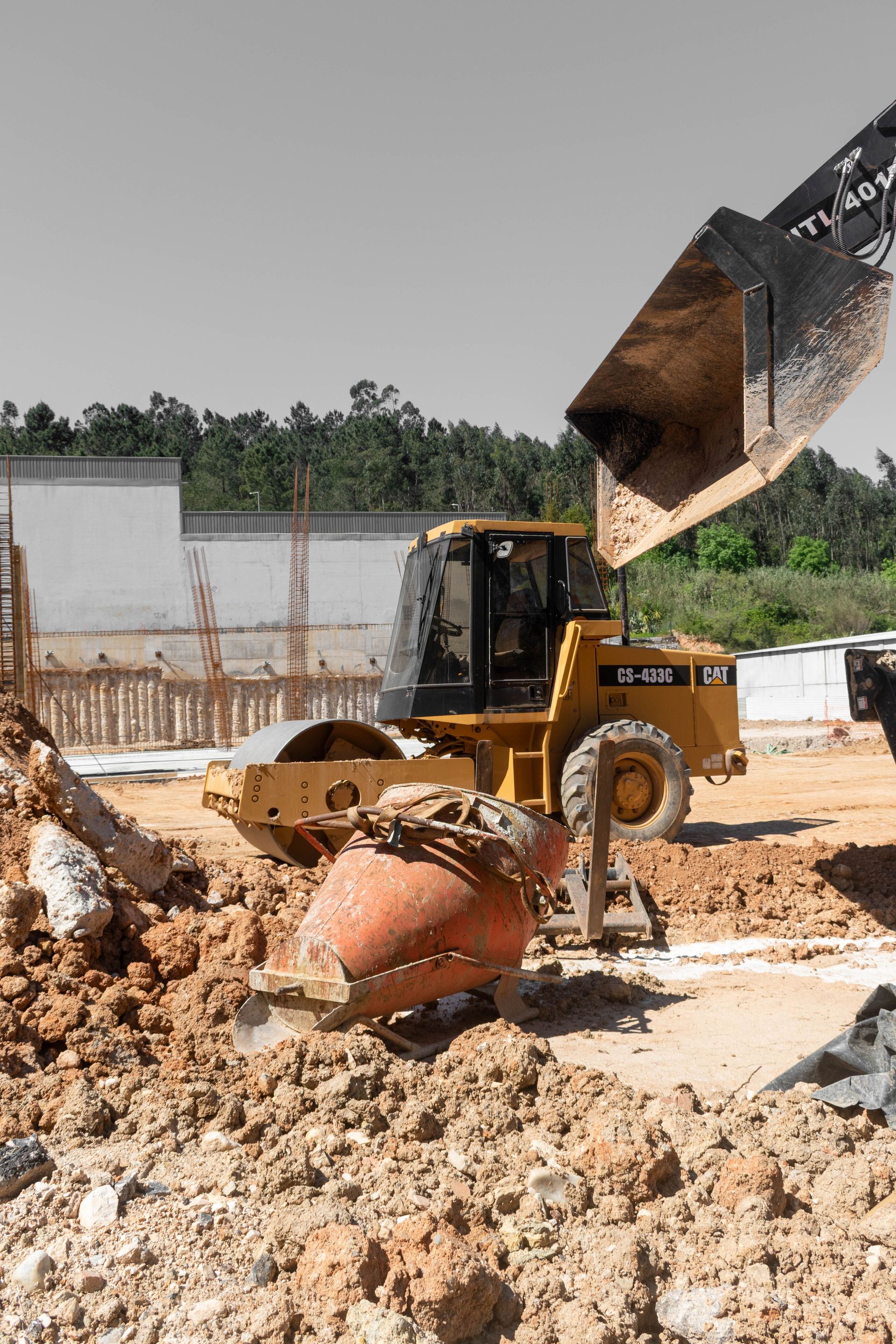 Yellow excavator dumping dirt at a muddy construction site with piles of soil and concrete debris