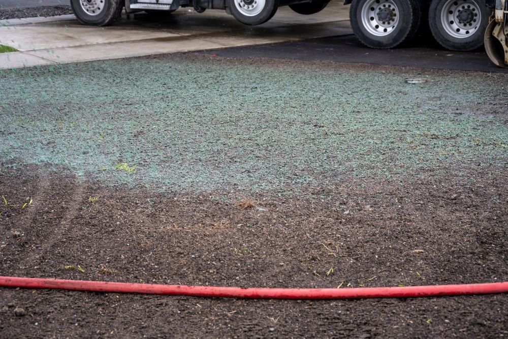 Gravel lot with a red hose in the foreground and truck wheels parked along the top edge
