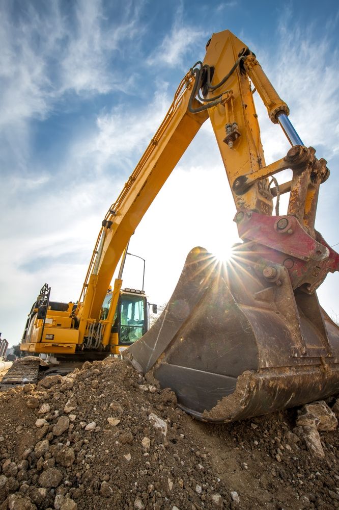 Yellow excavator digging a mound of dirt under a bright sky with sun glare