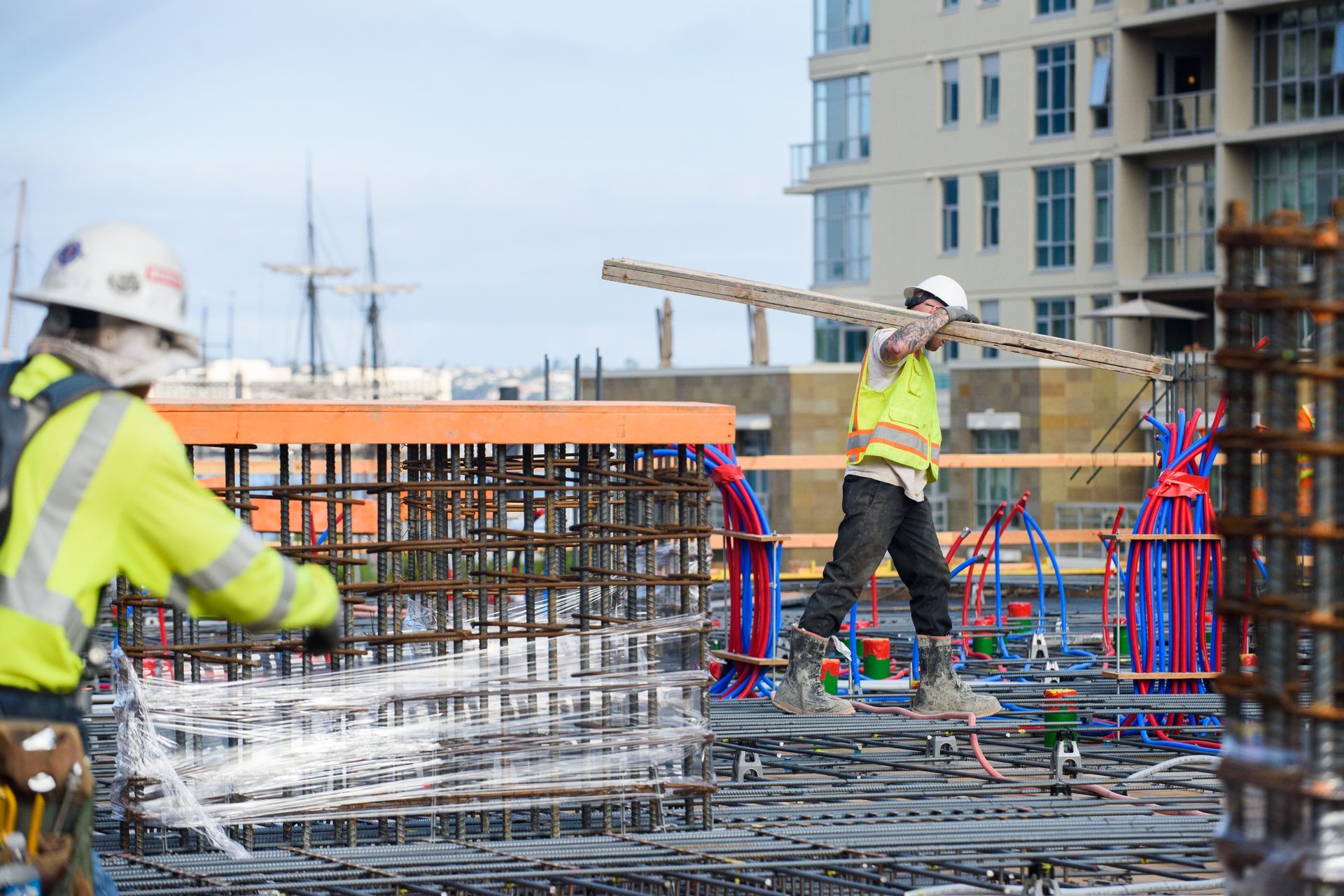 Construction workers in safety vests and hard hats at a rebar site near a waterfront building