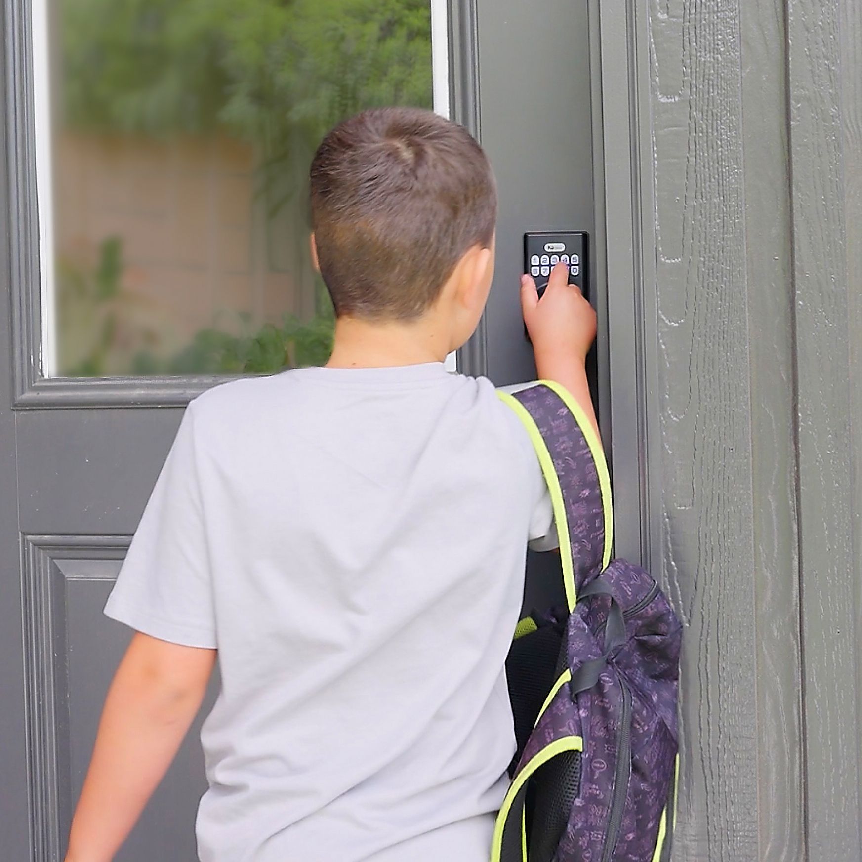 Person using a keypad to enter a building next to a gray door, with a backpack on one shoulder