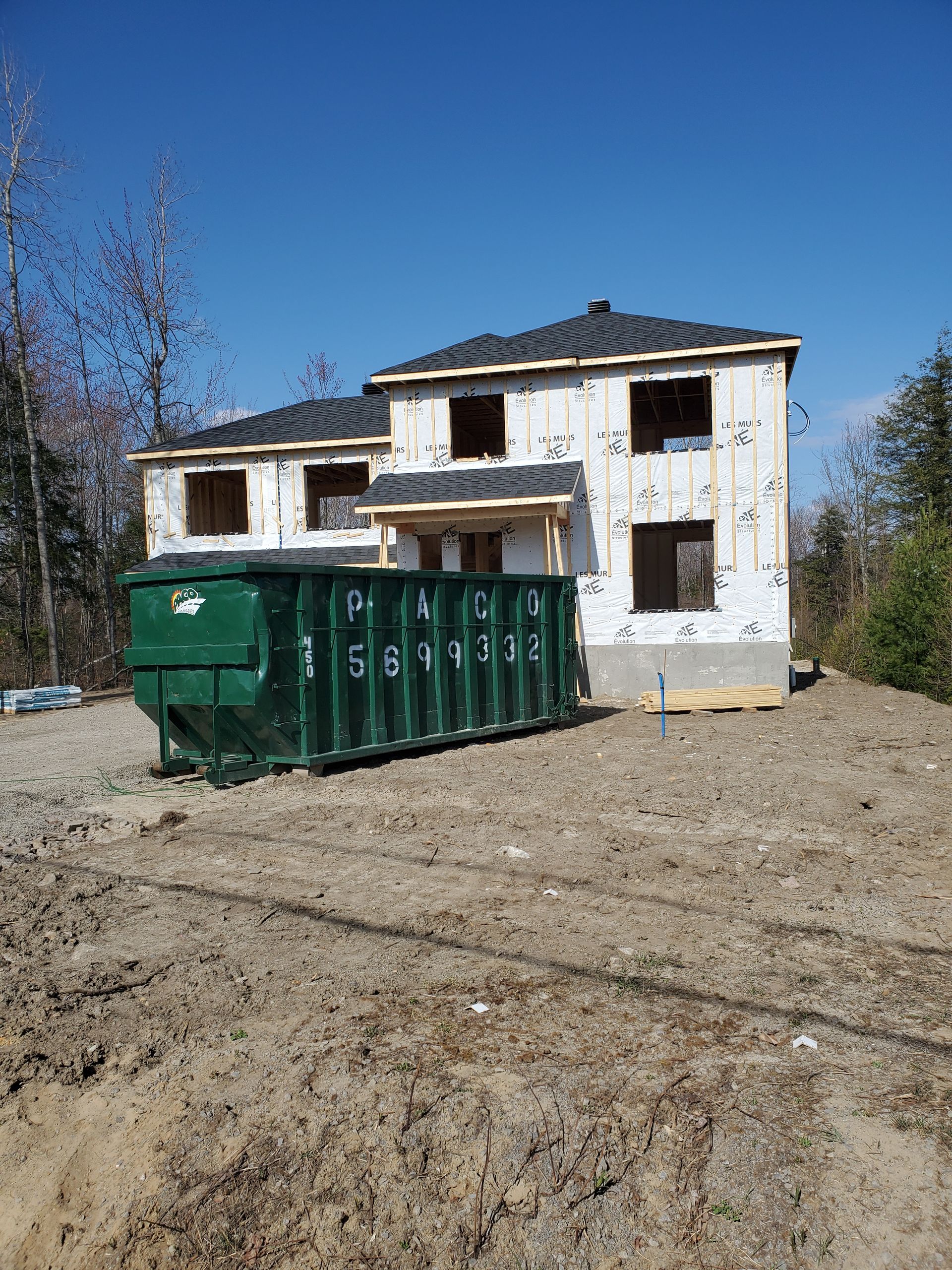 Une grande benne verte se trouve devant une maison en construction.