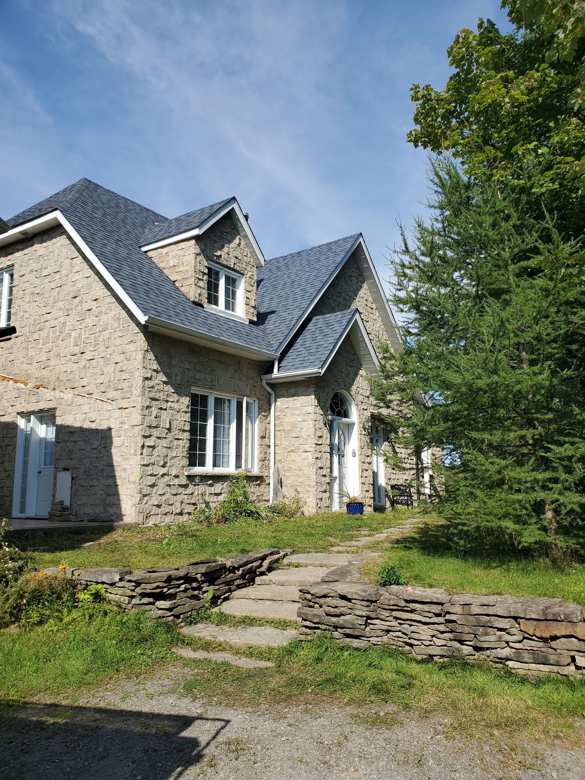 Une grande maison en briques avec un toit bleu est entourée d'arbres et d'herbe.