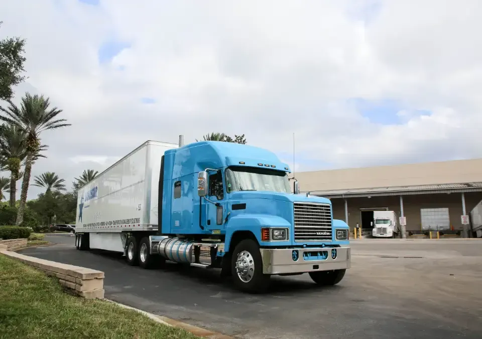 A light blue truck pulling a large white shipping trailer.