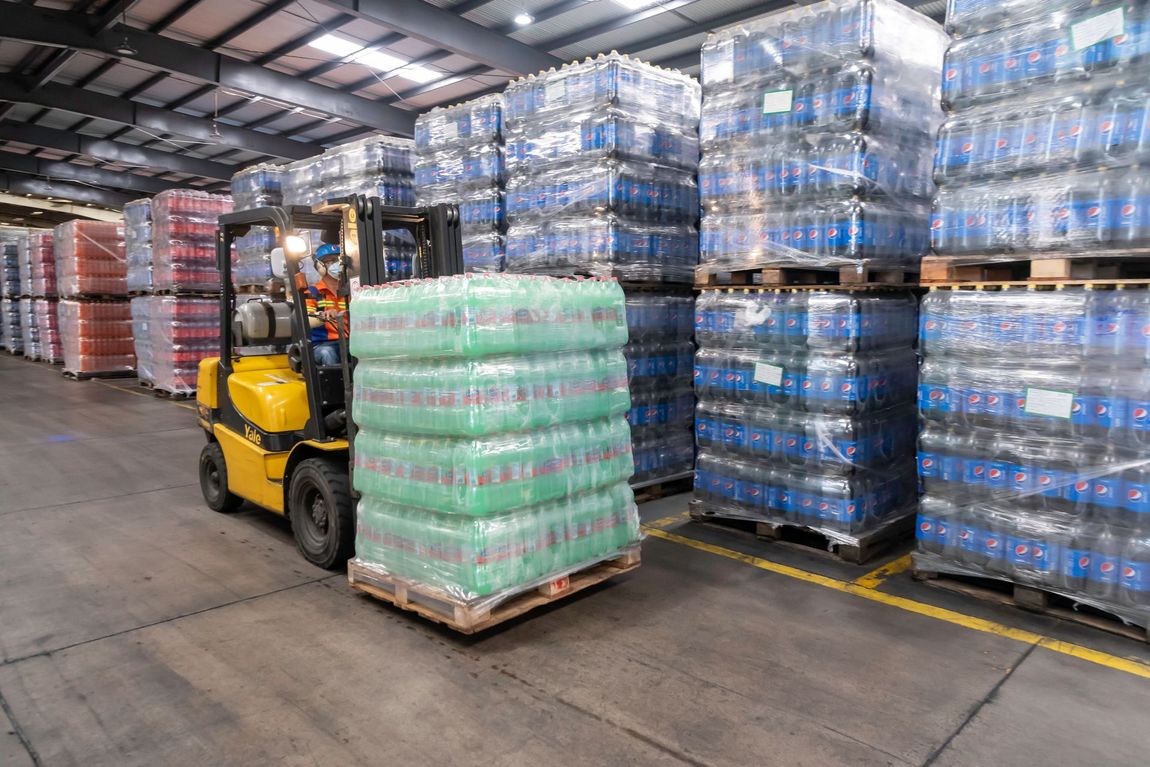 A person forklifting a pallet of soda bottles