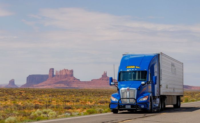 A blue freight truck with red mountains in the background.