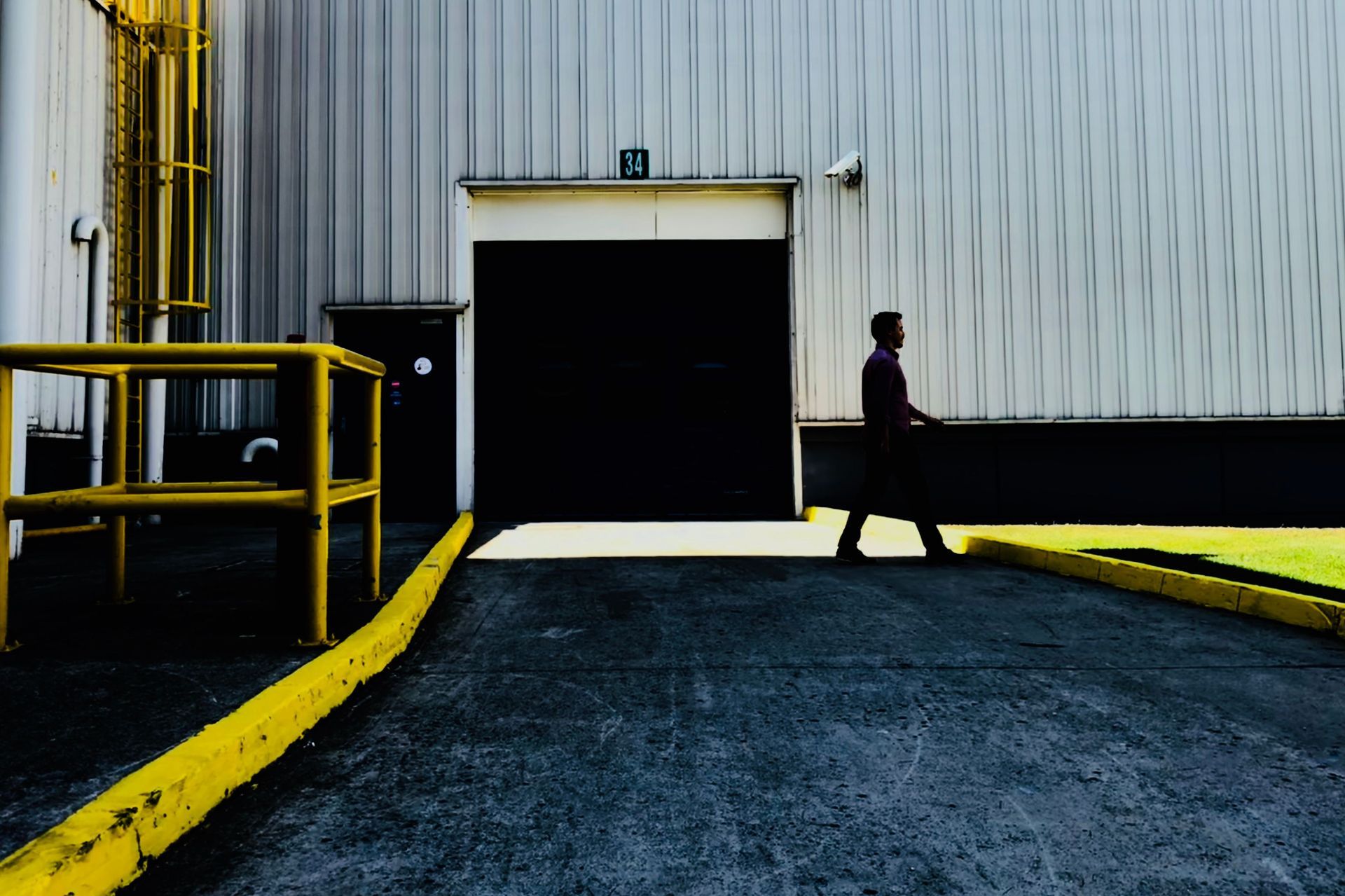 A person walking next to a shipping dock inside of a warehouse.