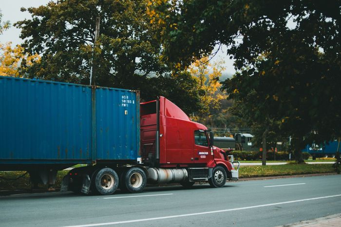 A red freight truck carrying a blue shipping container