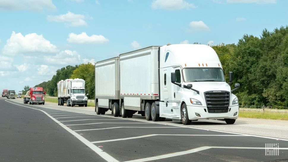 A white truck pulling two white trailers on the highway.