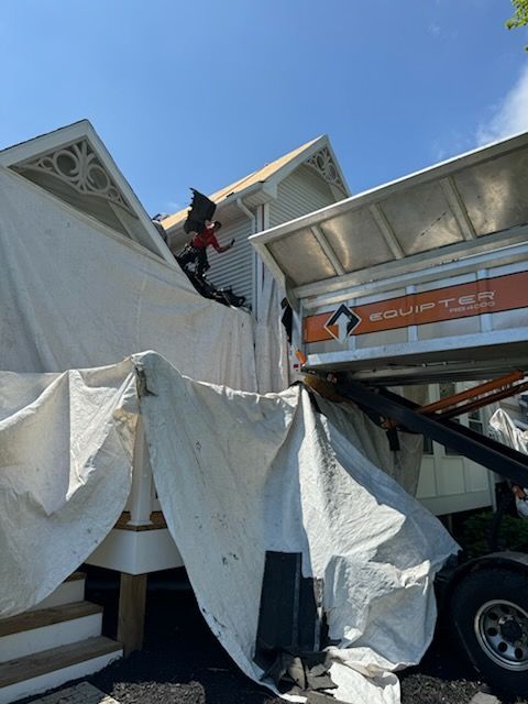 A man is standing on the roof of a house next to a truck.