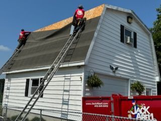 Two men are working on the roof of a white house.
