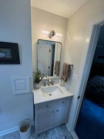A bathroom with a sink , mirror and trash can.