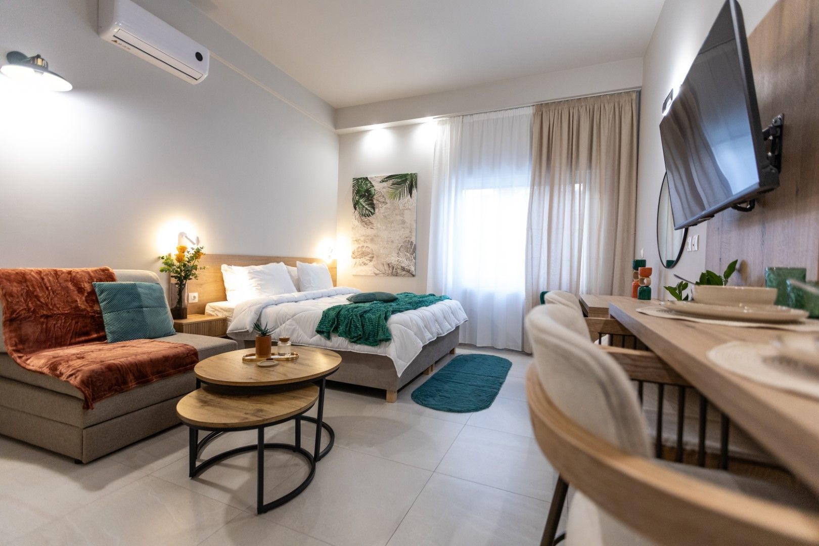 Cozy studio apartment with bed, small sofa, desk, and TV; light colors, wooden accents.