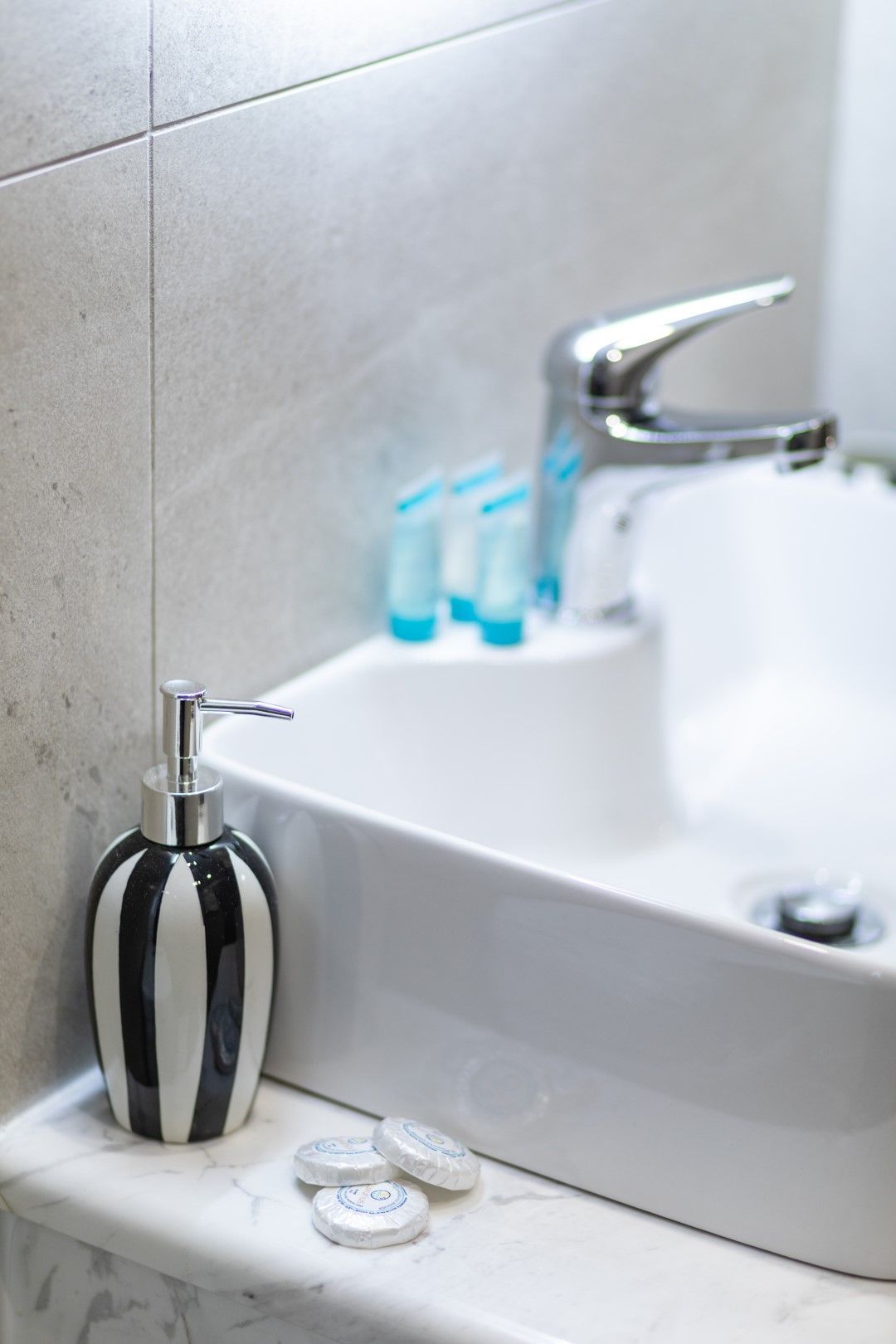 Bathroom sink with chrome faucet, black and white striped soap dispenser, and small toiletries.