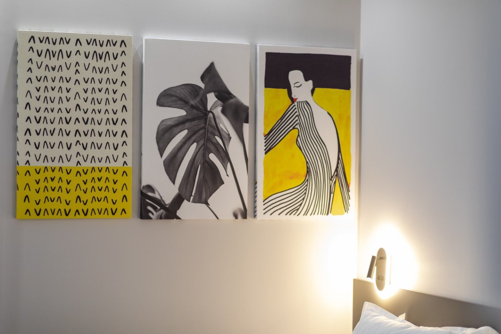 Three colorful art prints on a gray wall: patterned abstract, monstera leaf, and a woman in a yellow dress.