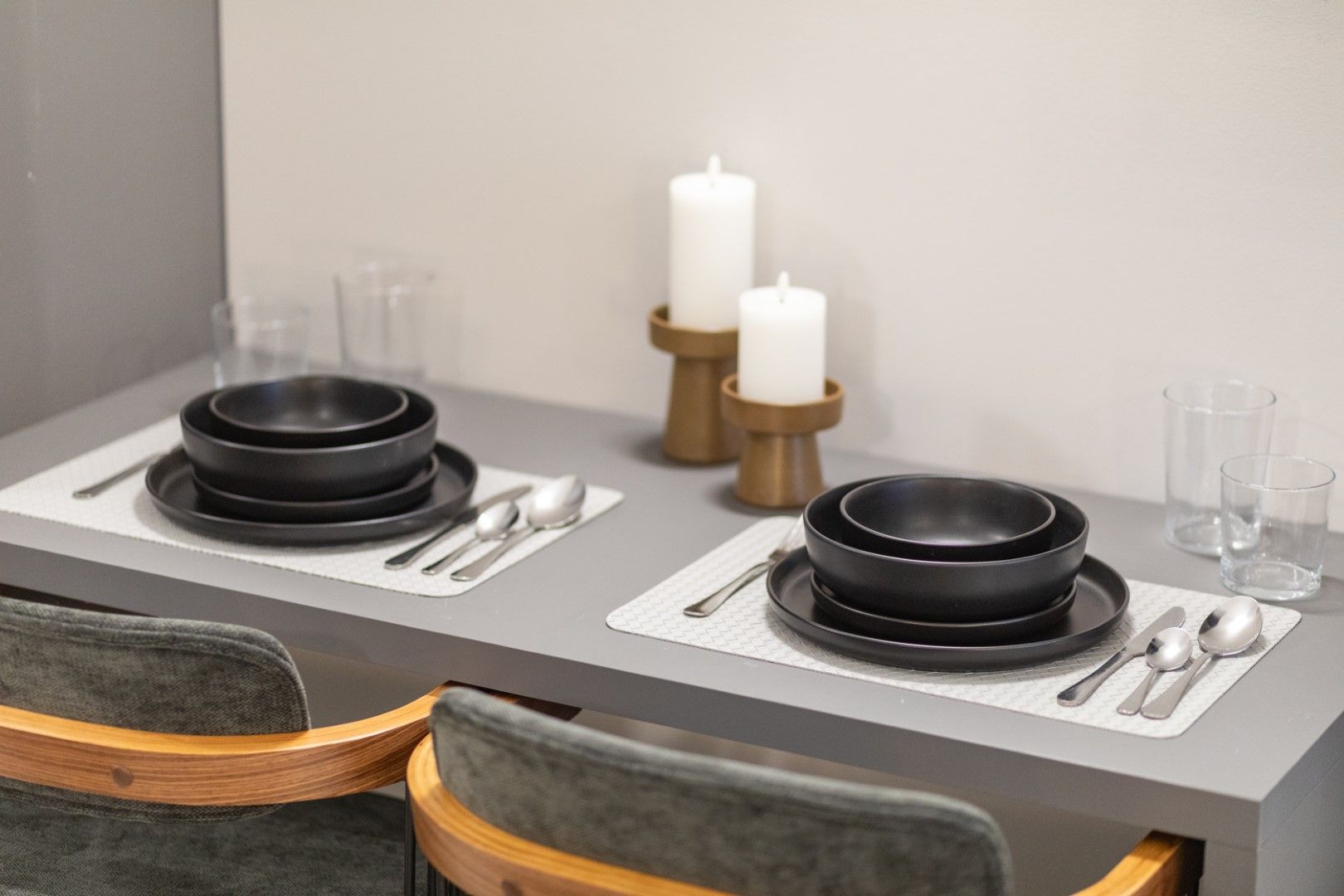 Two place settings with black bowls, silverware, and candles on a gray table.