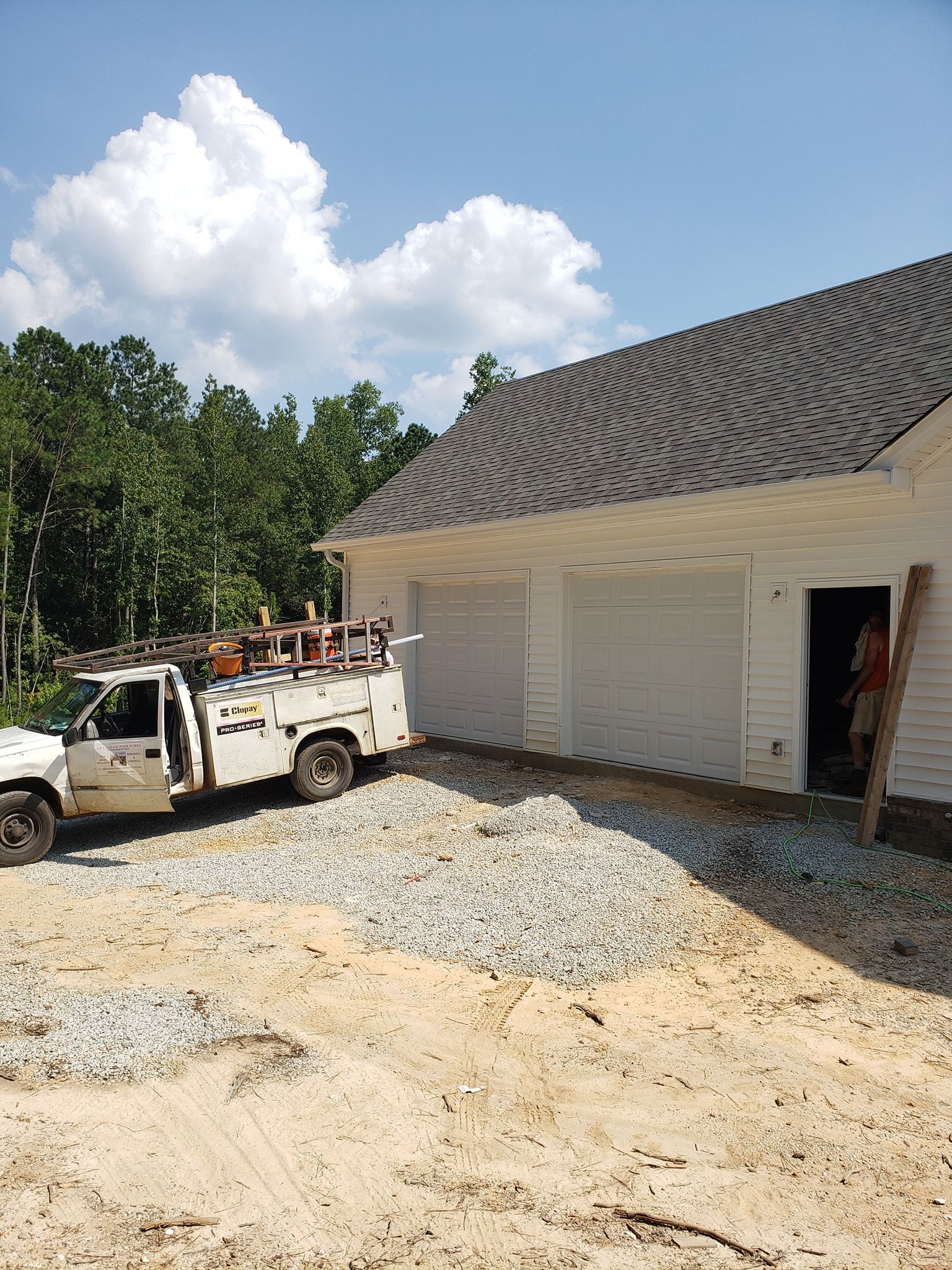 White work truck parked next to a partially built building. Gravel and sand ground. Blue sky with clouds.
