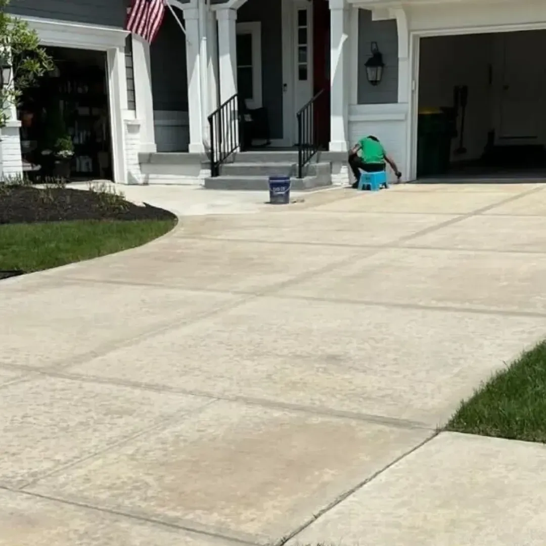 Person on driveway near house, cleaning. Concrete driveway, lawn, American flag, garage.