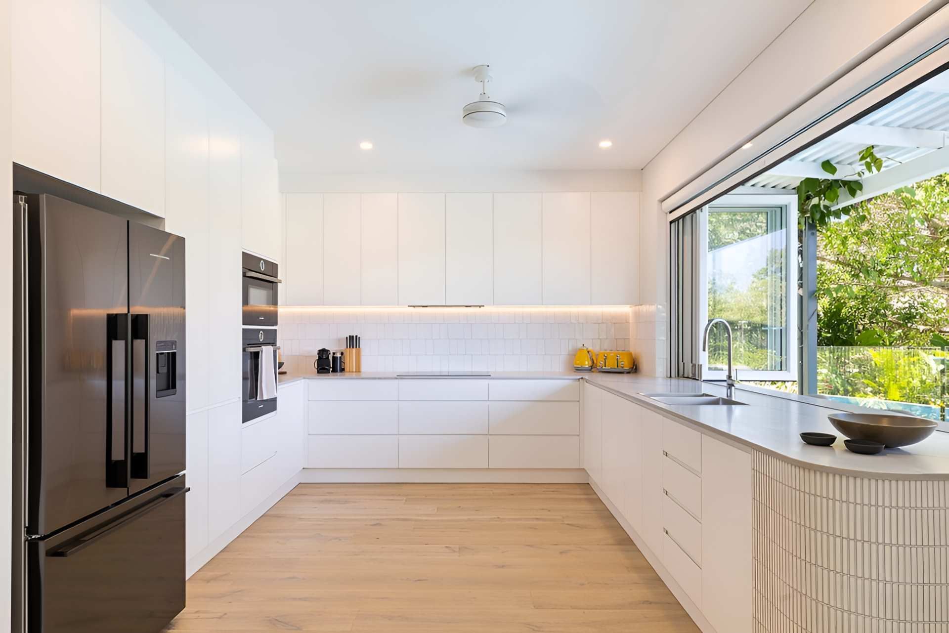 A Kitchen With White Cabinets and Black Appliances and a Large Window — Kitchens by CCJS in Bungalow, QLD