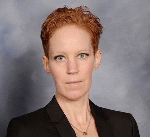Studio portrait of a person with short red hair in a black blazer against a gray background